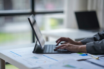 Close up of a businesswoman working on a tablet with charts and documents on a white table