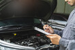 © Pormezz - Auto check up and car service shop concept. Mechanic writing job checklist to clipboard to estimate repair quotation to client at workshop garage.