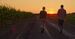 © StockMediaSeller - Silhouettes of two farmers walking side by side along a country road beside fields at sunset.