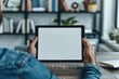 © dashtik - Man Holding Blank Tablet Screen in Modern Home Office Workspace with Bookshelf in Background