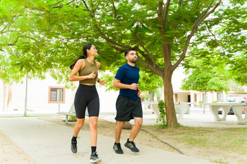 full length view of a man and a woman joggging together in a city park with trees, enjoying their da
