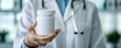 © Cheewynn - Close-up of a doctor holding an unbranded medicine container, clean and minimalistic medical environment