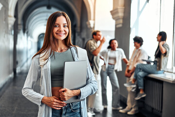 Portrait of confident motivated modern smiling female college student holding laptop and smiling. Concept of education and student life.