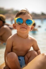 Wall Mural - A toddler wearing sunglasses sits on the beach. AI.