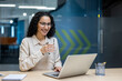 © Liubomir - Confident professional woman smiling at laptop screen in modern office. Holding water, enjoying break. Scene captures productivity, relaxation, modern work environment.