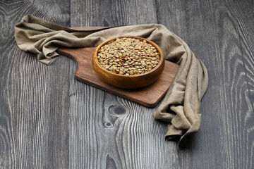 Green lentils in wooden bowl on wooden table background. Top view, copy space. Flat lay.