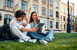 © HBS - Two young students are sitting on the grass on the campus talking and preparing for classes. Real student life.