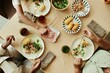 © Seventyfour - Top view of unrecognizable Black family eating balanced meal with corn, sausages and fresh salad at dining table with beige tablecloth