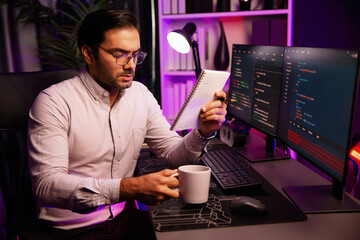 Smart IT developer working with coffee on software development coding on pc screen, reading note with newest application project program update online website data at neon light cyber office. Surmise.