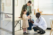 © pressmaster - Smiling young girl visiting a pediatric clinic, interacting with a friendly doctor, holding medical equipment while her mother oversees situation