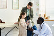 © pressmaster - Child receiving medical attention from doctor while parent watches Briefcase on table and medical equipment visible in background
