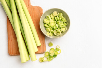 Board and bowl with slices of fresh leek on white background