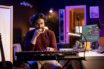 Wall Mural - Male artist composing music on electronic piano keyboard in home recording studio. Sound engineer playing MIDI controller, working on producing a soundtrack with acoustic tools and gear.