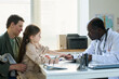 © pressmaster - Child accompanied by parent during medical appointment, consulting with doctor in clinical office, holding a soft toy, engaging in conversation, displaying calm and attentive expressions