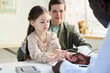 © pressmaster - Smiling girl and parent sitting in doctor's office during medical appointment, with healthcare professional holding girl's hand. Scene capturing candid moments in medical setting