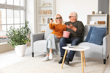 Wall Mural - Mature couple in 3D glasses with popcorn watching movie on sofa at home