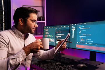 Smart IT developer working with coffee on software development coding on pc screen, reading note with newest application project program update online website data at neon light cyber office. Surmise.