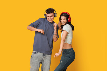 Wall Mural - Beautiful young couple in headphones dancing on yellow background