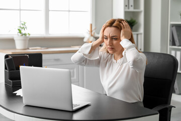 Canvas Print - Adult woman suffering from headache with laptop in office