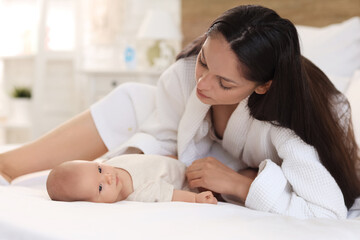 Sticker - Beautiful young woman in bathrobe with her baby lying on bed at home