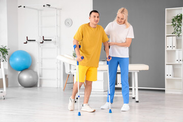 Poster - Young man with crutches and physiotherapist walking in rehabilitation center