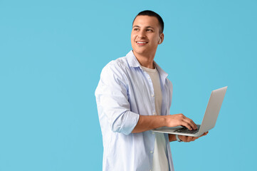 Handsome young happy man with laptop on blue background