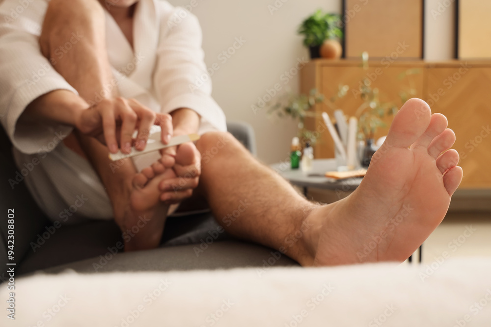 Handsome young man with file doing pedicure at home, closeup