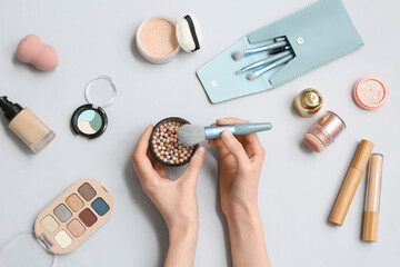 Wall Mural - Female hands with powder pearls, makeup brush and different cosmetic products on grey background