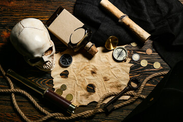 Skull with rum, compasses, coins and paper on dark wooden background. Pirate concept