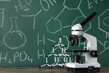 Wall Mural - Modern microscope and molecular model on wooden table near chalkboard with chemical formulas