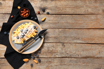 Wall Mural - Delicious Belgian waffles with berries, nuts and sugar powder on plate on wooden background. Top view