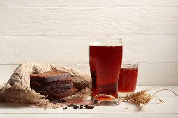 Glasses of fresh kvass with slices of bread and wheat on white wooden background