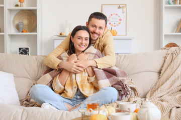 Wall Mural - Happy young couple with plaid sitting at home on autumn day