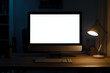 © kiewkoii - Dimly lit workspace with a blank computer screen, keyboard, and desk lamp, creating a quiet and focused environment for late-night work.