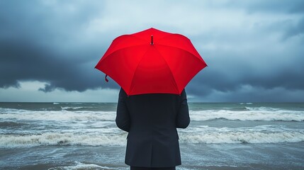 Poster - Rear view of a businessman standing in stormy seaside in cloudy day while holding red umbrella 