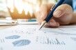 © Tonton1541 - A close-up of a hand holding a pen, analyzing charts and graphs on paper, ideal for business and finance themes.