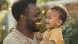 © Elena - Radiant African American Father Embracing Joyful Toddler Son Outdoors