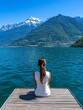 © TingeGlint - A serene view of a woman relaxing on a dock by a lake with stunning mountain scenery in the background.