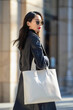 © Agata25 - Attractive Asian woman in stylish coat walking with white tote bag on urban street