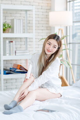 Wall Mural - Asian young woman beautiful female happy smiling enjoying  with decorative makeup, beauty products, and cosmetics while sitting on white bed, Concept of teenage lifestyle at home