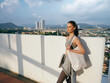 © SHOTPRIME STUDIO - Young woman standing on a rooftop with a cityscape background, wearing casual athletic clothing and holding a tote bag