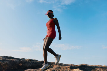 Wall Mural - Woman in a red athletic outfit walking on rocks under a clear blue sky