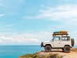 © Mnt - A vintage off-road vehicle parked on a scenic cliffside, overlooking a stunning ocean view under a clear blue sky.