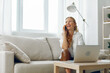 © SHOTPRIME STUDIO - Woman multitasking at home, working on laptop and talking on phone while sitting on a comfortable couch