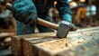 © Thaweechai - A close-up of a hammer driving a nail into wood, with a worker's determined expression visible in the background