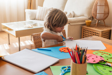 Kid Making Halloween Decorations With Scissors, Surrounded By Craft Supplies.