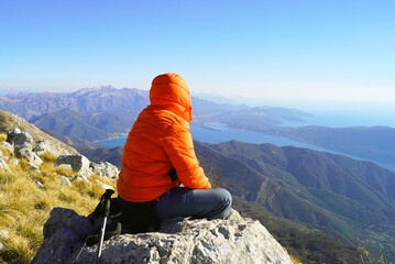 Wall Mural - A tourist in a colorful jacket enjoying the breathtaking view of the Montenegrin coast from Mount Orjen. A man sitting on a rock and resting after climbing to the top of Radostak in the Bay of Kotor