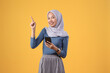 © Ibenk.88 - happy asian indonesian muslim woman holding smart phone with pointing finger gesture on isolated yellow background