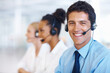 © STEEXBuyout/peopleimages.com - Man, portrait and smile in call center for customer support, telemarketing and FAQ in office. Male consultant, happy and headset at help desk with team, communication or bilingual agent with tech