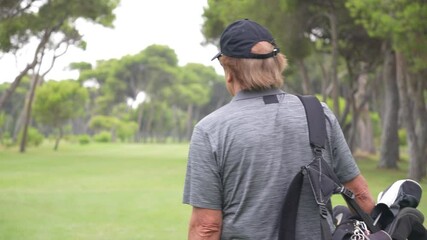 Wall Mural - A man wearing a hat and carrying a golf bag walks across a green golf course. Concept of leisure and relaxation, as the man is likely taking a break from his golf game to enjoy the outdoors